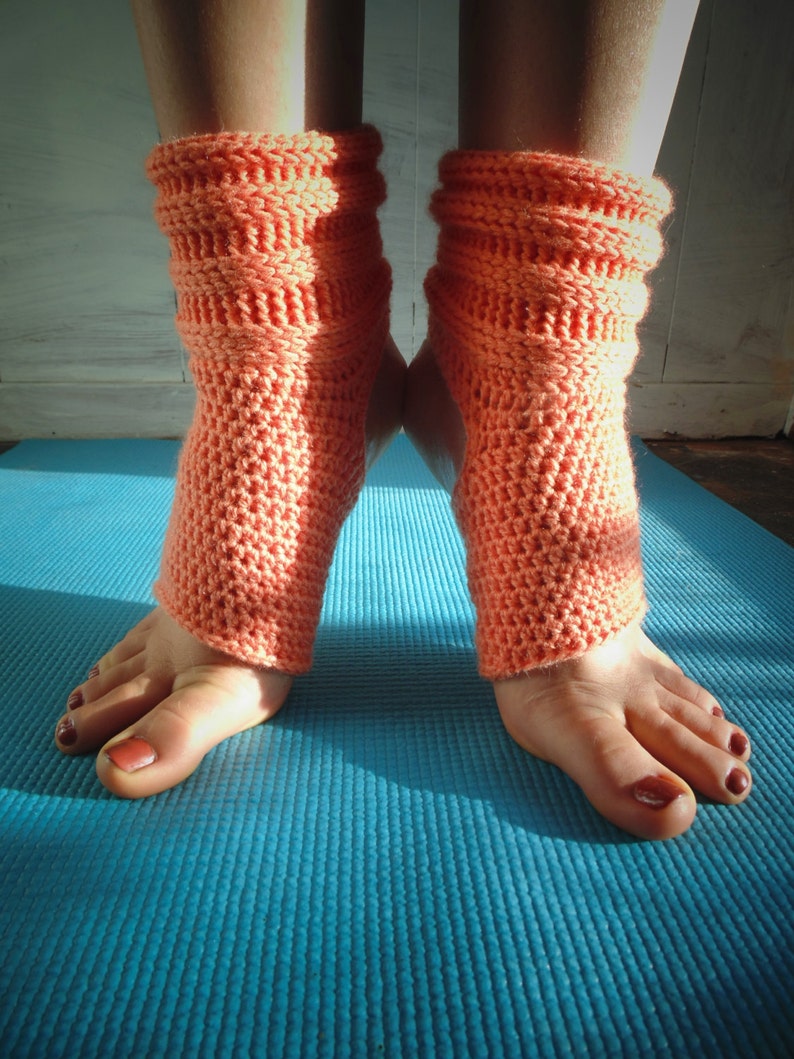 May include: A pair of coral-colored crocheted ankle warmers on a blue yoga mat.