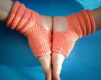 May include: A pair of coral-colored crocheted ankle warmers with a hole for the heel. The warmers are worn on a person's feet and are shown against a blue background.