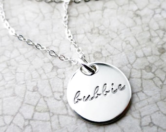May include: A silver necklace with a round pendant that says "bubbie" in cursive.