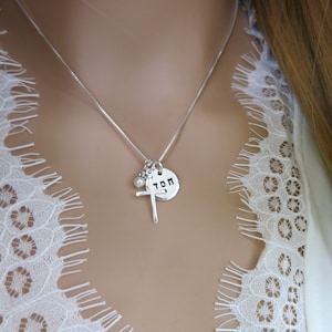 May include: A silver necklace with a cross charm, a small pearl charm, and a round charm with the word "TOM" engraved on it.