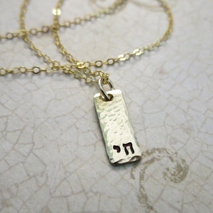 Op de afbeelding: Gouden ketting met een gehamerde gouden hanger met het Hebreeuwse woord "Chai" in zwarte letters.