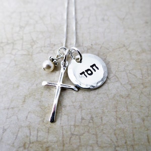 May include: Silver necklace with a small pearl charm, a cross charm, and a round charm with the word "TOM" inscribed on it.
