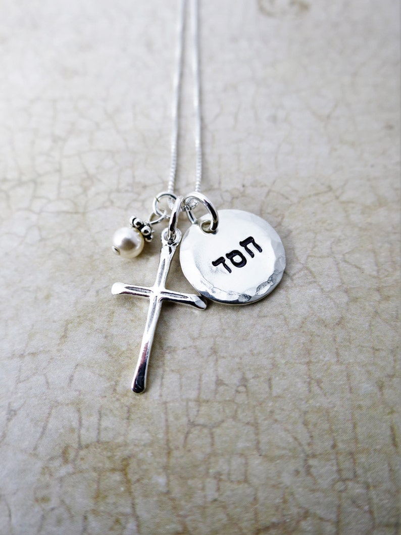 May include: Silver necklace with a small pearl charm, a cross charm, and a round charm with the word "TOM" inscribed on it.
