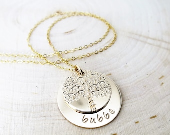 May include: Gold necklace with a round pendant featuring a tree design and the word "bubbe" engraved on the bottom.