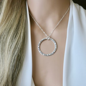 Puede incluir: Un collar de plata con un colgante circular inscrito con texto hebreo. El colgante tiene un diámetro de aproximadamente 3,8 cm.