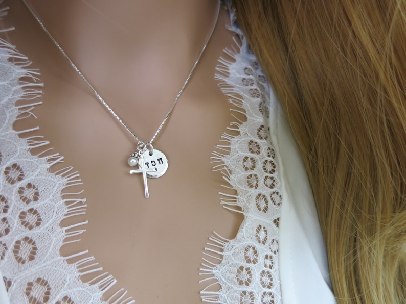 May include: A silver necklace with a cross charm, a small pearl charm, and a round charm with the word "TOM" engraved on it.