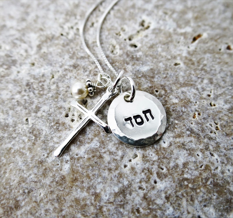 May include: Silver necklace with a cross charm, a small pearl, and a round pendant with the Hebrew word "TOV" inscribed on it.