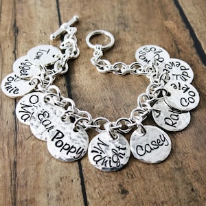 May include: Silver charm bracelet with multiple personalized charms, including the names Tom, Roger, Annie, Mia, Oscar, Poppy, Dwight, Casey, Rat, Coo, Zip, and Boss.