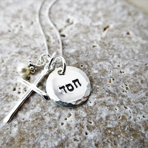 May include: Silver necklace with a hammered silver disc pendant that says "TOM" in Hebrew. The necklace also features a small silver cross with a pearl bead.