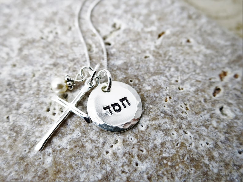 May include: Silver necklace with a hammered silver disc pendant that says "TOM" in Hebrew. The necklace also features a small silver cross with a pearl bead.