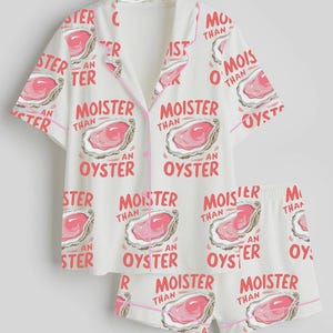 May include: White pajama set with a pink oyster print and the text "MOISTER THAN AN OYSTER". The set includes a short-sleeved button-up shirt and matching shorts, both trimmed with pink piping.