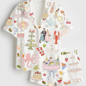 May include: White pajama set with a whimsical print featuring wedding-themed illustrations. The short-sleeved top and shorts display images of cakes, champagne, a bride and groom, and other celebratory elements. The set has pink trim.