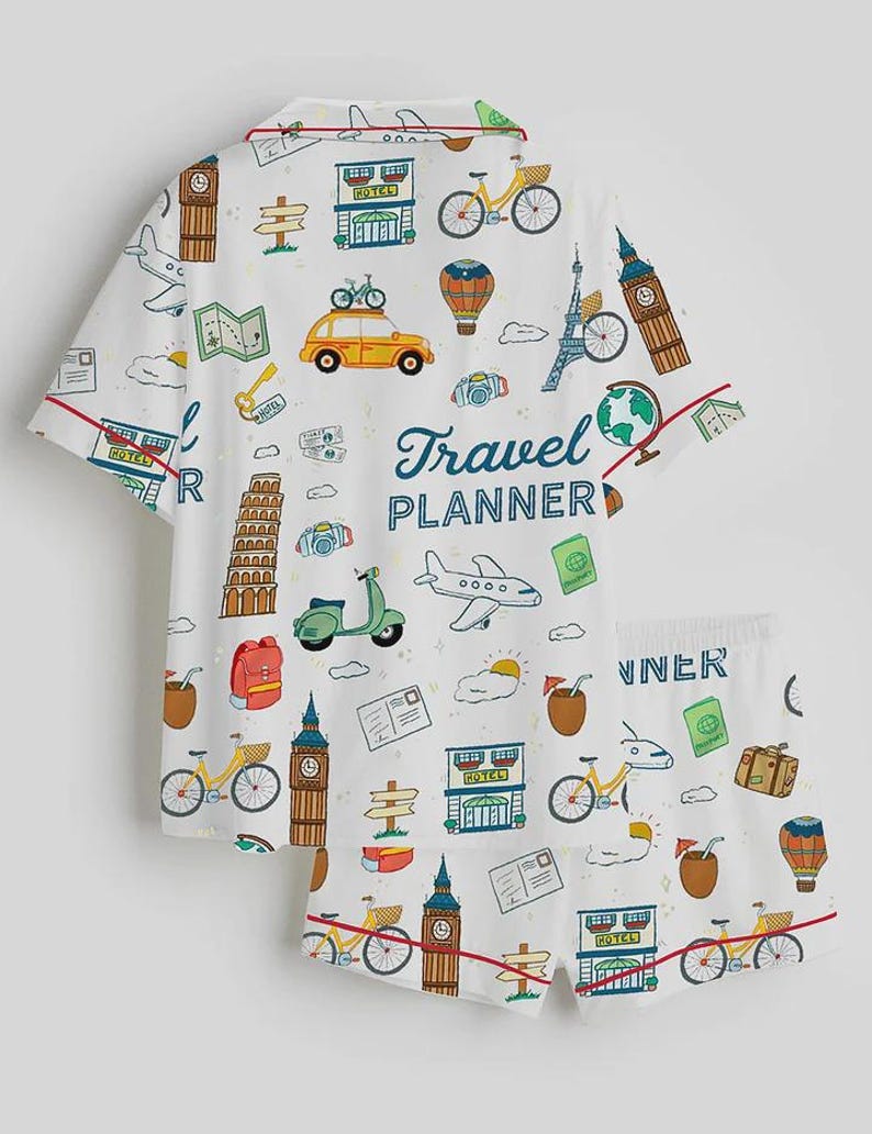 Puede incluir: Conjunto de pijama blanco con estampado de tem&aacute;tica de viajes. La camiseta de manga corta y los pantalones cortos presentan ilustraciones de monumentos, veh&iacute;culos e iconos de viaje. Las palabras "Travel Planner" est&aacute;n impresas en la parte superior.