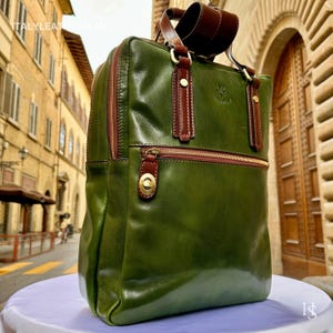 Puede incluir: Mochila de cuero verde con detalles marrones, asa superior y bolsillo frontal con cremallera. La bolsa tiene herrajes dorados y un logotipo. El texto "ITALYLEATHERMAN" es visible en la parte superior.