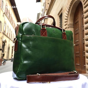 Può includere: Una cartella in pelle verde scuro con manici in pelle marrone, una tracolla marrone abbinata e finiture color ottone. La borsa ha una forma rettangolare con una tasca frontale e un piccolo logo in rilievo sul lato destro.