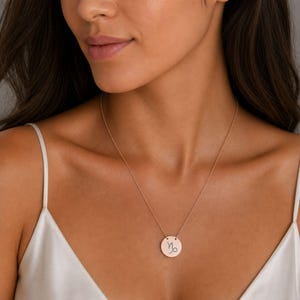 Pu&ograve; includere: Una collana con ciondolo circolare color oro rosa che presenta il simbolo zodiacale del Capricorno inciso al centro. Il ciondolo pende da una sottile catenina abbinata, poggiando sulla zona della clavicola di un top bianco.
