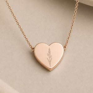 May include: A rose gold heart-shaped pendant necklace featuring a delicate, thin-line engraving of a single flower stem with small blossoms centered on the front surface, suspended from a matching fine link chain.