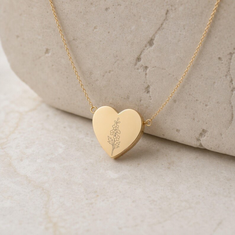 Puede incluir: Un collar con colgante en forma de coraz&oacute;n de tono dorado que presenta un delicado dise&ntilde;o floral grabado con l&iacute;neas finas en la parte frontal. El colgante cuelga de una cadena fina a juego, sujeta a los lados superiores del coraz&oacute;n.