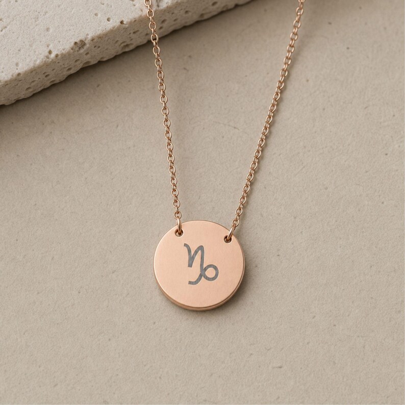 Pu&ograve; includere: Una collana color oro rosa con un ciondolo circolare inciso con il simbolo zodiacale del Capricorno. Il ciondolo &egrave; sospeso a una sottile catenina abbinata, creando un design semplice e pulito che mette in risalto la finitura metallica.