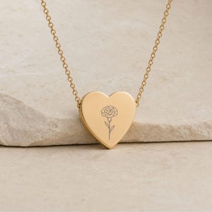 Close-up of the engraved carnation heart pendant on a gold necklace, the January birth flower design