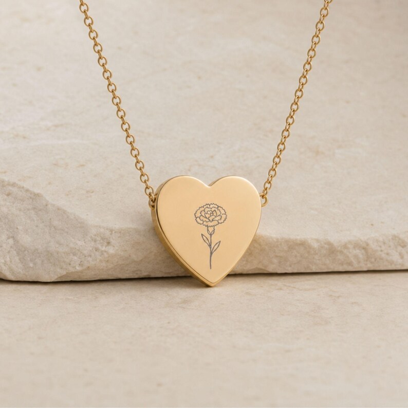 Close-up of the engraved carnation heart pendant on a gold necklace, the January birth flower design