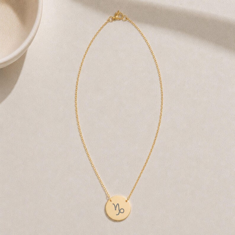 Pu&ograve; includere: Una collana color oro con una catenina sottile e un ciondolo circolare. Il ciondolo &egrave; inciso con il simbolo zodiacale del Capricorno in un carattere scuro e contrastante. La collana presenta un piccolo moschettone di chiusura in alto.