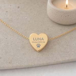 May include: A gold-toned heart-shaped pendant necklace featuring the engraved text LUNA, the phrase Always With Me, and a small paw print icon. The pendant is attached to a delicate gold-toned chain, creating a simple and elegant piece of jewelry.