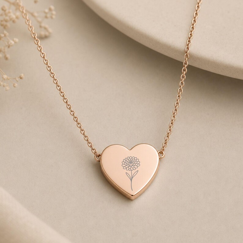 K&ouml;nnte beinhalten: Eine herzf&ouml;rmige Anh&auml;ngerkette aus Ros&eacute;gold mit einer zarten, d&uuml;nnen Kette. Der zentrale Herzanh&auml;nger ist mit einer einzelnen, detaillierten Strichzeichnung einer Blume graviert. Das Metall hat eine glatte, polierte Oberfl&auml;che.