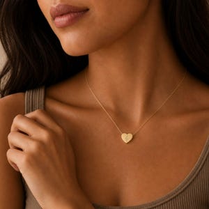 Pu&ograve; includere: Una collana con ciondolo a forma di cuore color oro, caratterizzata da una piccola e delicata incisione di un rametto botanico al centro del cuore. Il ciondolo pende da una sottile catenina color oro abbinata che poggia sulla clavicola.