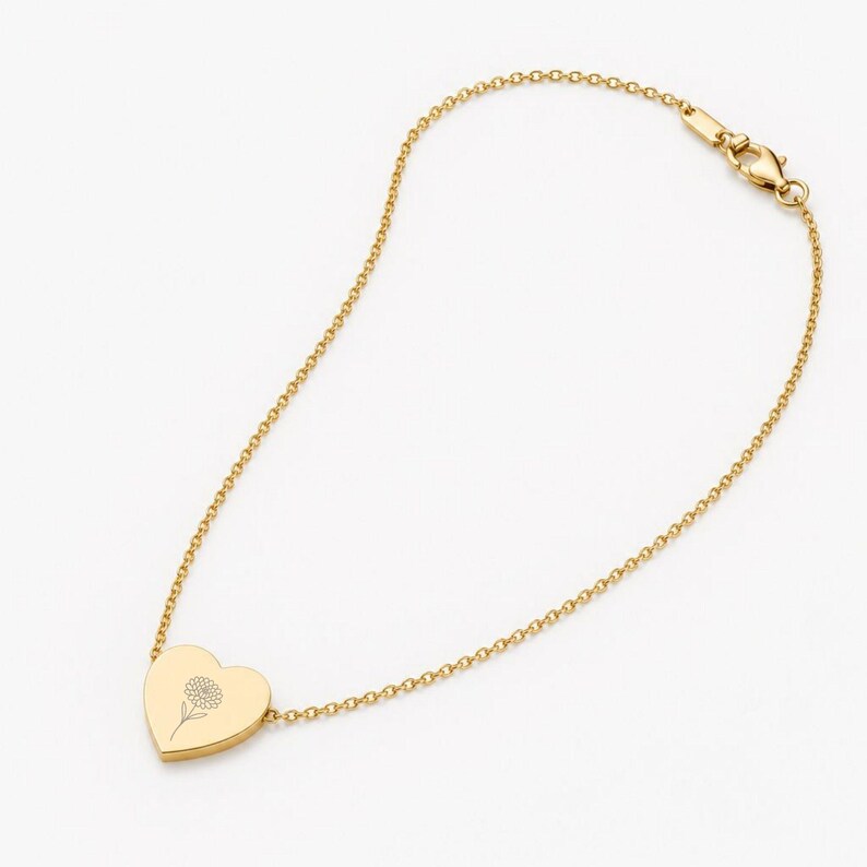 K&ouml;nnte beinhalten: Ein goldfarbenes Kettenarmband mit einem herzf&ouml;rmigen Anh&auml;nger. Der Anh&auml;nger ist mit einer feinen Strichzeichnung einer Blume graviert. Das Armband verf&uuml;gt &uuml;ber einen Karabinerverschluss am Ende der d&uuml;nnen, polierten Metallgliederkette.