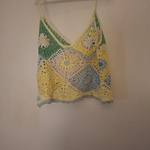 Pode incluir: Uma regata de crochê sem mangas com um design de patchwork de motivos quadrados em amarelo pastel, verde claro e azul suave. A peça tem um decote em V profundo, alças finas e uma bainha festonada, feita de fio.