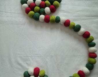 Puede incluir: Una guirnalda decorativa de bolas de fieltro en forma de espiral. La guirnalda presenta bolas de fieltro rojas, blancas y verdes. Las bolas de fieltro están dispuestas en espiral, con una cadena de bolas que se extiende desde la espiral.