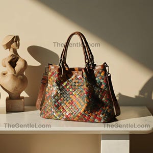 Puede incluir: Un bolso de mano de cuero trenzado multicolor con un mosaico de cuadrados rojos, verdes, amarillos y azules. El bolso tiene dos asas de cuero marrón, una correa de hombro extraíble y el texto TheGentleLoom impreso en la parte frontal.