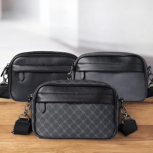 以下が含まれることがあります： 木製の表面に、調節可能なストラップが付いた3つの黒いクロスボディバッグが表示されています。 バッグは角が丸い長方形の形をしています。 1つのバッグは幾何学模様で、他のバッグは無地の黒とグレーです。