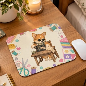 May include: A rectangular mouse pad featuring a cream-colored background with a repeating pattern of sewing supplies including scissors, spools of thread, buttons, and fabric. In the center, a cartoon corgi wearing sunglasses operates a sewing machine.