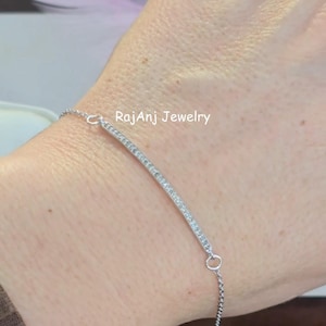 Może przedstawiać: Srebrna bransoletka z zakrzywionym paskiem z małych, przezroczystych kamieni. Bransoletka jest na nadgarstku, z widocznym tekstem "RajAnj Jewelry". Bransoletka jest delikatna i wydaje się być wykonana z metalu.