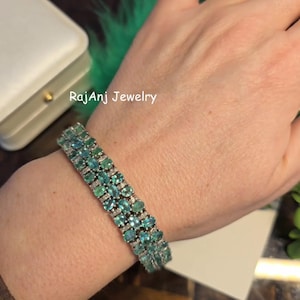 May include: A gemstone bracelet with rows of oval-cut, teal-colored stones and small, clear accent stones. The bracelet is on a person's wrist. The text "RajAnj Jewelry" is visible in the background.