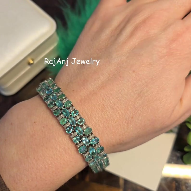 May include: A gemstone bracelet with rows of oval-cut, teal-colored stones and small, clear accent stones. The bracelet is on a person's wrist. The text "RajAnj Jewelry" is visible in the background.