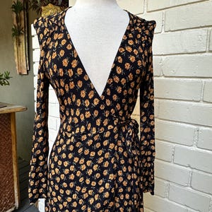 May include: A long-sleeved wrap dress with a V-neckline and a black background with a small, yellow floral pattern.