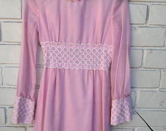 May include: A long-sleeved pink dress with white lace trim around the neckline, cuffs, and waist. The lace features a scalloped edge and a repeating circle pattern.