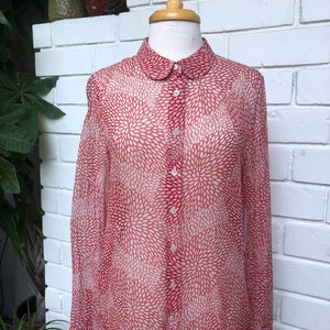 May include: A red and white patterned sheer button-up shirt with a peter pan collar.