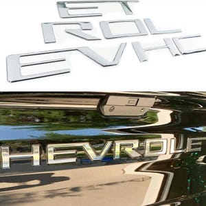 May include: A set of individual chrome-finished letters spelling out CHEVROLET, shown both as separate pieces and applied to the black tailgate of a vehicle. The letters have a reflective metallic surface and a bold, block-style font design.