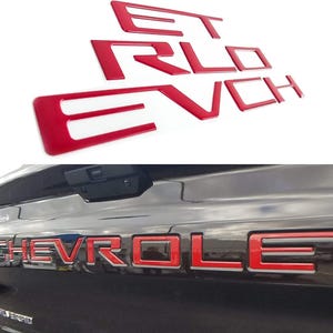 May include: A set of bright red, three-dimensional adhesive letters that spell out CHEVROLET. The letters are designed to be applied to the tailgate of a vehicle, as shown in the lower portion of the image where the red letters are installed.