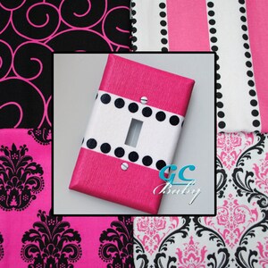 May include: Pink and white light switch cover with black polka dots. The cover is made of fabric and has a textured surface. The switch is in the center of the cover. The text "GC Baby" is in the lower right corner of the image.