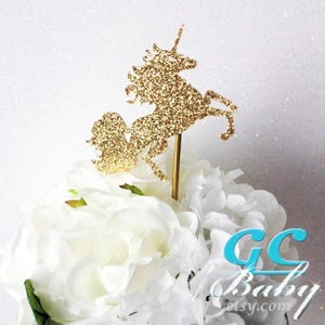 Op de afbeelding: Gouden glitter unicorn taarttopper. De unicorn staat op zijn achterpoten met zijn hoofd naar achteren gekanteld. De unicorn staat op een gouden stok.