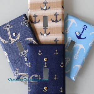 May include: A collection of nautical-themed light switch covers. The covers feature anchor patterns in various colors, including navy blue, light blue, and tan. Some covers have gold-colored screws and a rectangular opening for the switch.
