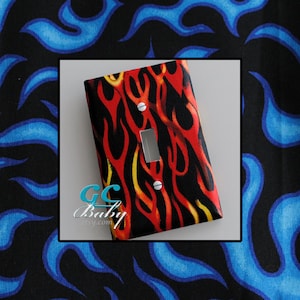 May include: A light switch cover with a red, yellow, and black flame pattern. The cover is made of fabric and has a white switch plate.