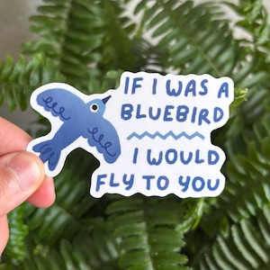 May include: A sticker featuring a bluebird illustration with the text "If I was a bluebird I would fly to you" in blue lettering. The sticker is held in front of a background of green leaves.