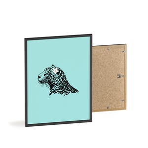 Könnte beinhalten: Ein gerahmter Kunstdruck mit einer schwarz-weißen Illustration eines Jaguarprofils auf hellblauem Hintergrund. Das Kunstwerk befindet sich in einem schwarzen Rahmen, wobei die Rückseite eines anderen Rahmens sichtbar ist.