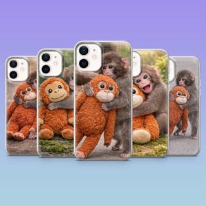 May include: Phone cases featuring images of monkeys hugging orange plush monkeys. The cases have a clear border and a glossy finish. The background of the images on the cases is a natural setting.
